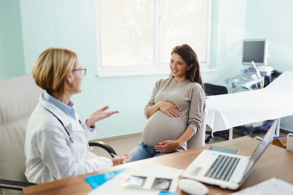 Happy pregnant woman talking to her gynecologist in the office.